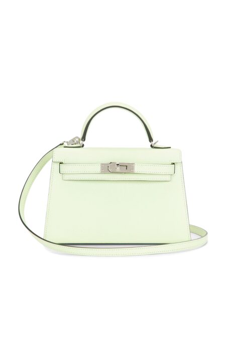 Front view of a mini trapezoidal pale mint green structured calfskin handbag featuring a structured top handle, silver-tone turnlock closure, and a thin matching leather shoulder strap on a plain white background.