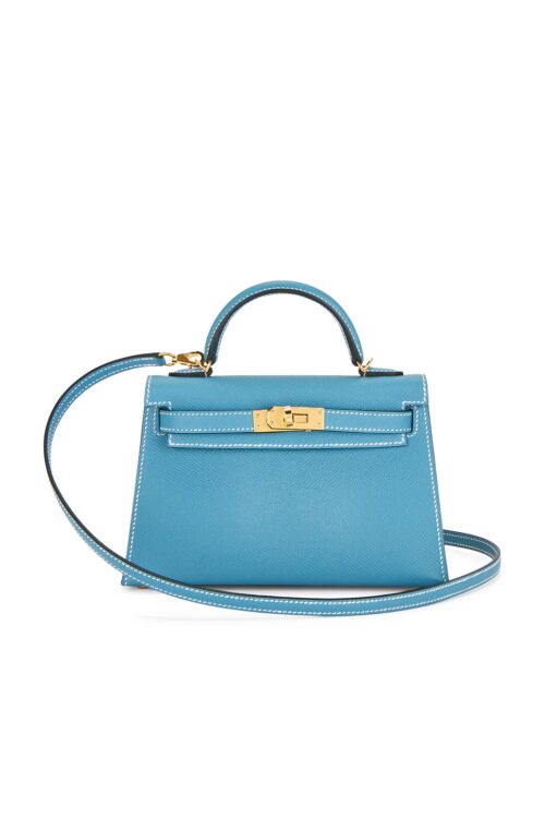 Front studio view of a bright blue structured leather mini top-handle handbag featuring gold-tone turnlock clasp, contrasting white stitching, and attached slender shoulder strap.