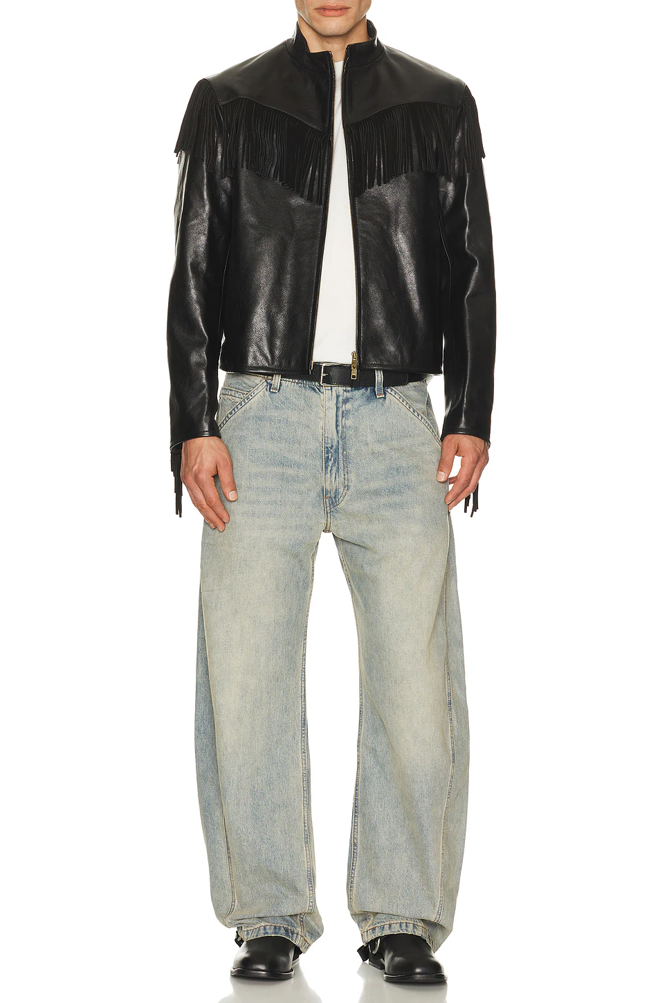 Full-length shot of a male model wearing a black fringed leather cafe racer jacket styled casually with loose-fit light wash blue jeans and black boots.
