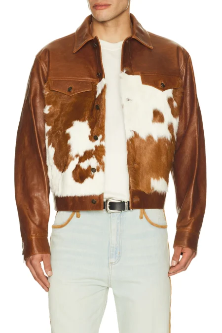 Front view torso close-up of a model wearing a brown leather trucker jacket with distinct brown and white cow fur panels on the front chest, styled with a white t-shirt and light-wash denim.