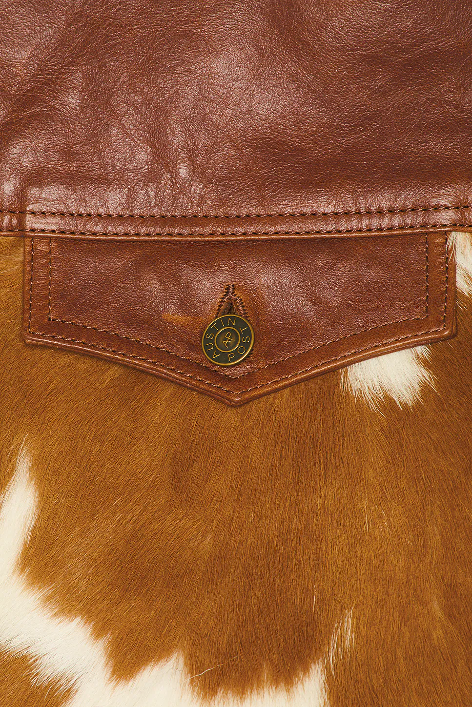 Detailed close-up showing the seam lines of a brown leather pocket flap, a textured brown-and-white cow fur panel, and a metallic button with embossed detailing.