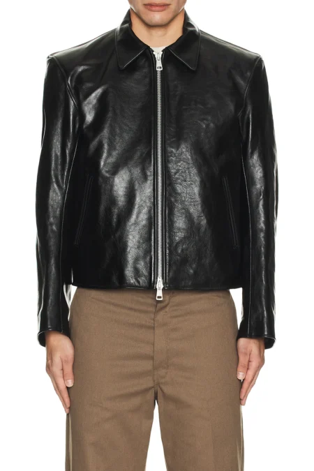 A direct front view of a model wearing a black structured leather jacket fully zipped, showcasing its smooth grain texture, side slant pockets, and clean lines.