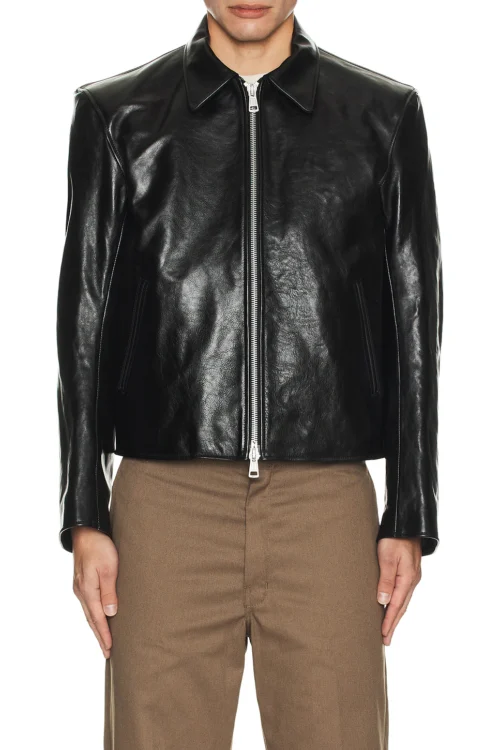 A direct front view of a model wearing a black structured leather jacket fully zipped, showcasing its smooth grain texture, side slant pockets, and clean lines.