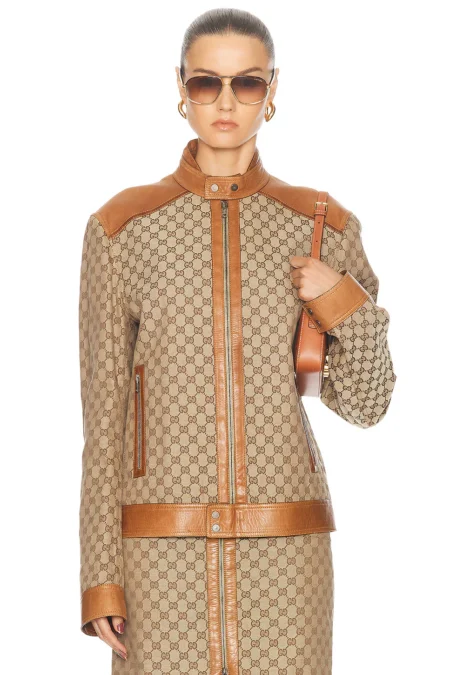 Front view of a model wearing a structured brown monogram canvas motorcycle jacket with tan leather panels on the shoulders, stand collar, cuffs, and front zip closure track.