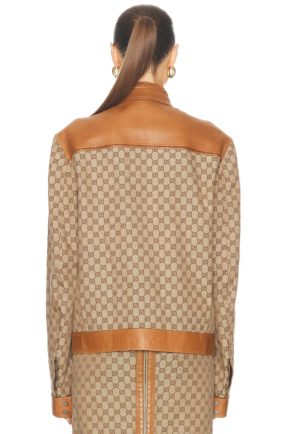 Rear view of a model in a patterned brown canvas jacket with a substantial tan leather yoke across the shoulders and a matching leather band at the lower hem.