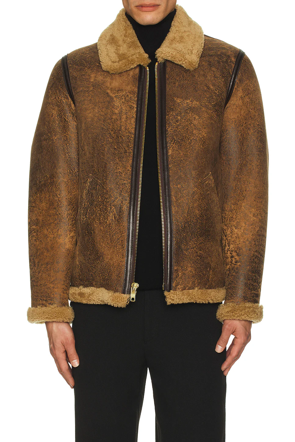 Model wearing a partially unzipped brown cowhide shearling jacket over a black turtleneck top, showcasing open shearling lapels and brass zipper detail.