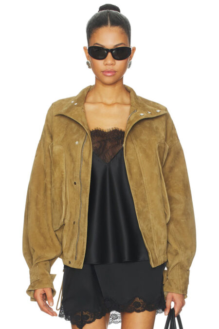 A model showcases a heavy brown goatskin suede coat worn unzipped, revealing its collar flaps, silver hardware, and clean inner construction.