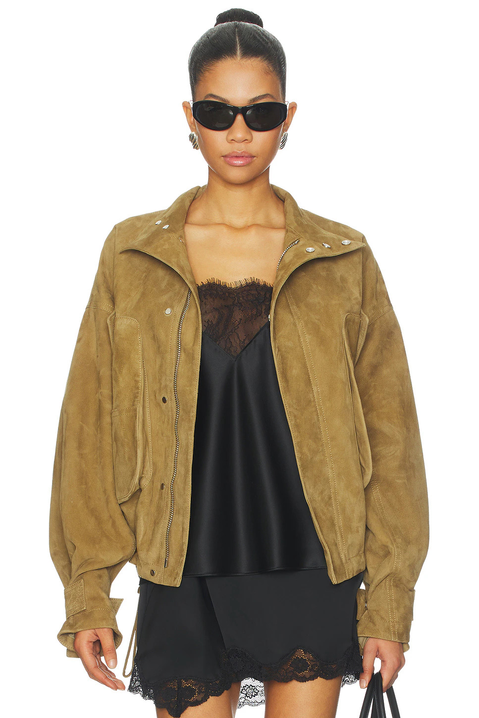 A model showcases a heavy brown goatskin suede coat worn unzipped, revealing its collar flaps, silver hardware, and clean inner construction.