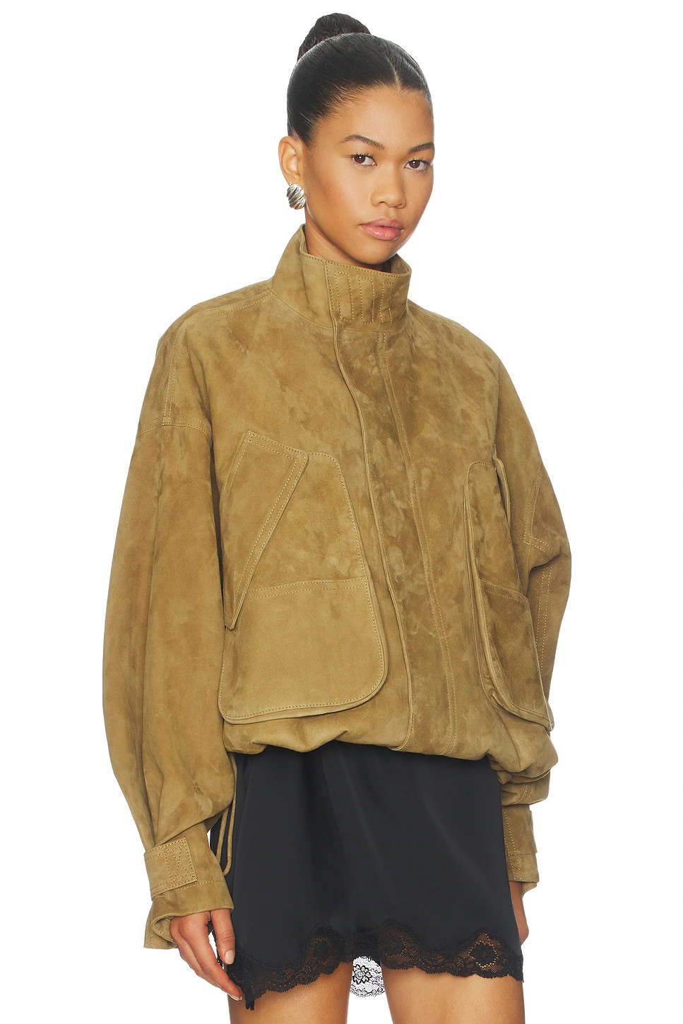 Three-quarter studio portrait of a woman wearing a high-collared tan suede bomber jacket with large utility pockets and slouchy dropped sleeves.