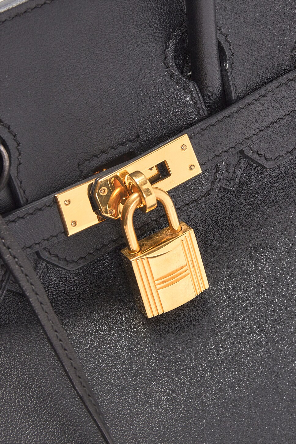 Macro close-up shot of an engraved gold-tone metal padlock attached to the central turnlock hardware on fine black calfskin leather.