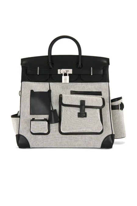 Front view of a multi-pocket luxury travel handbag crafted from cream and black woven canvas with black calfskin leather trim, featuring a top handle, a central silver padlock, multiple front slip pockets, and a matching bottle holder on the side.