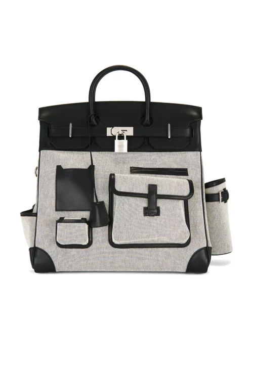 Front view of a multi-pocket luxury travel handbag crafted from cream and black woven canvas with black calfskin leather trim, featuring a top handle, a central silver padlock, multiple front slip pockets, and a matching bottle holder on the side.