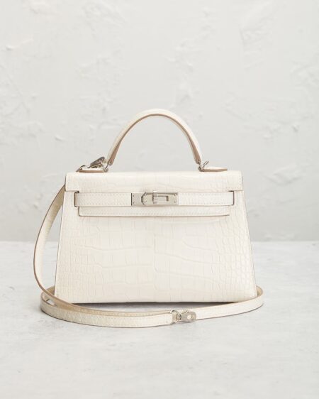 Front-facing white matte alligator leather handbag displayed in a lifestyle setting with structured top handle, detachable shoulder strap, polished silver-tone hardware, and elegant luxury styling.