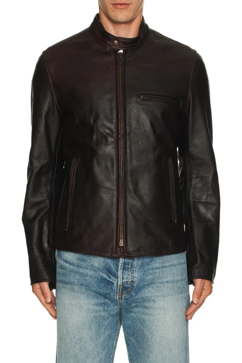 Cropped waist-up front view of a man wearing a zipped dark brown cowhide leather cafe racer jacket with a snap band collar, chest zip pocket, and side seam pockets paired with light wash denim jeans.