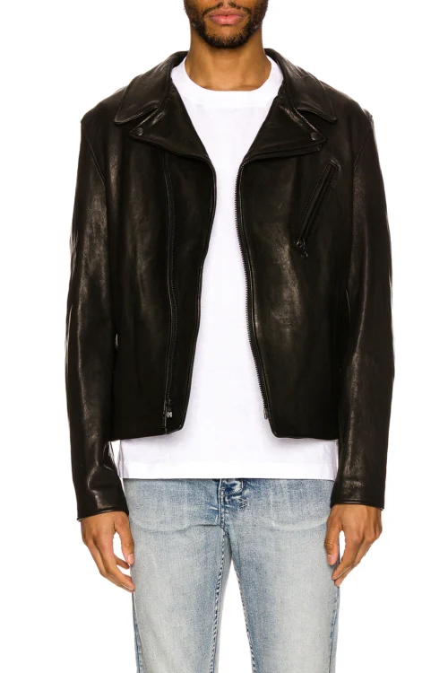 Cropped waist-up front view of a man wearing an open black lambskin leather perfecto jacket styled over a plain white t-shirt and light wash jeans, showing wide lapel collars, asymmetrical zipper tracks, and a slanted chest zip pocket.